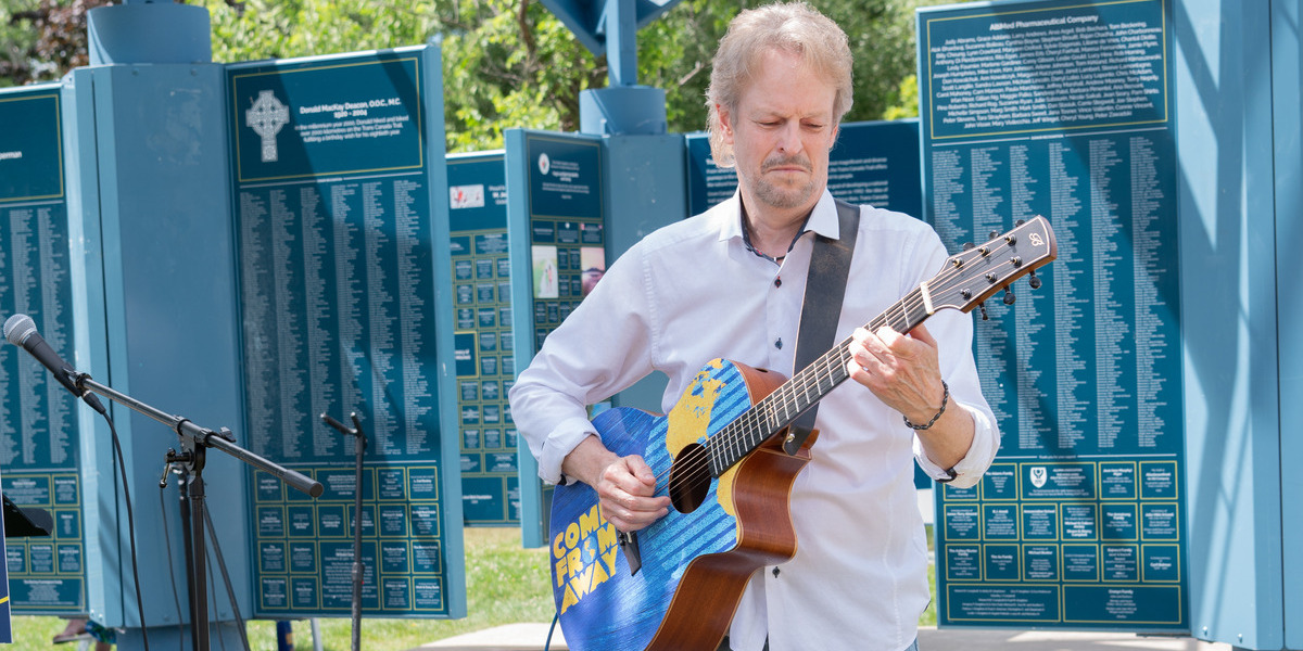 man playing accoustic guitar infront of trail signs on sunny day