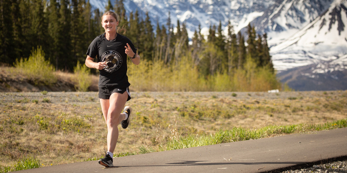 woman running on a trail with mountains behind