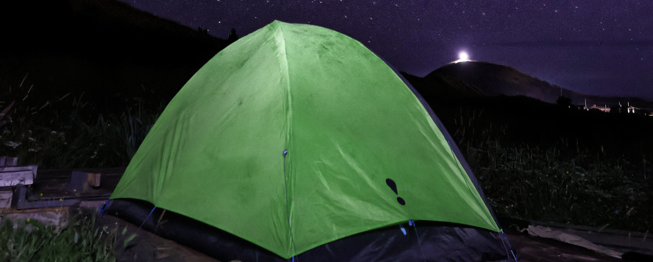 green tent at night on hill with moon and hill behind