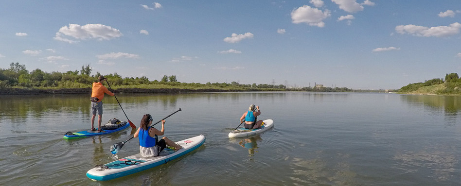 Three people paddling stand-up paddleboards on a waterway.