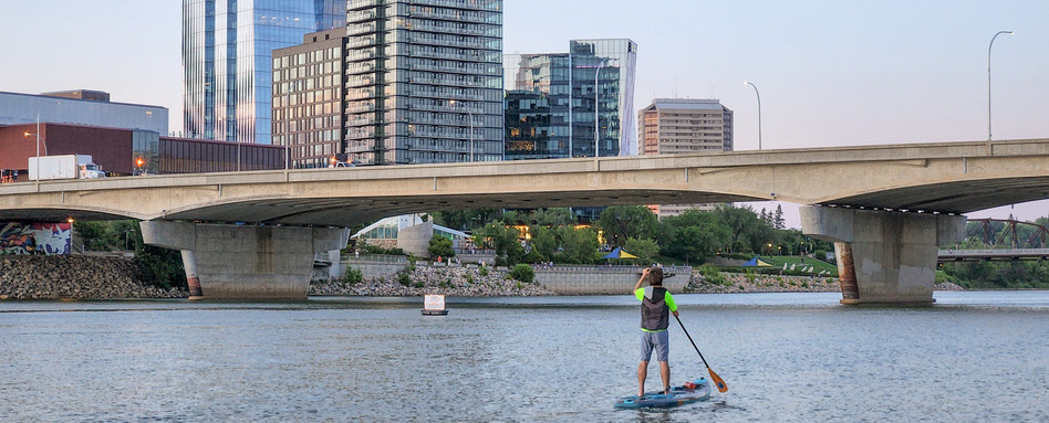A person standing on a paddleboard with a cityscape in the background.