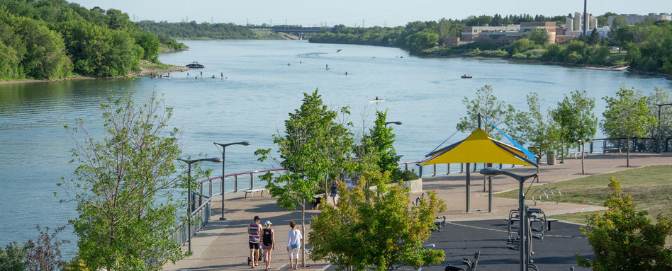 A walkway along the Saskatchewan River with paddlers visible in the distance.