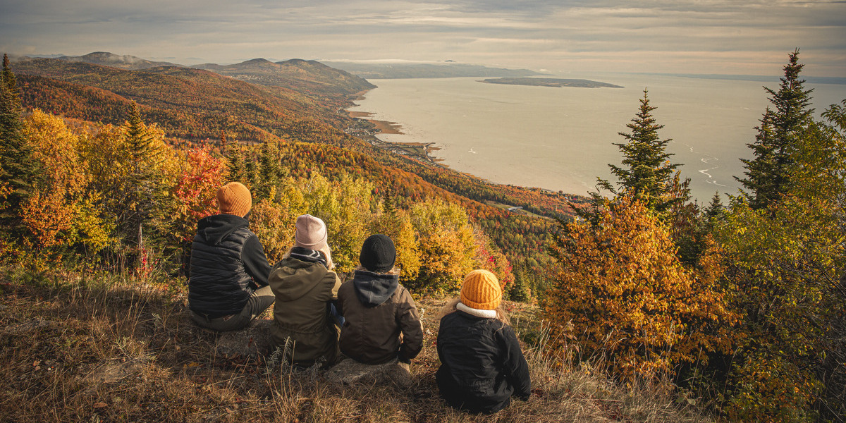 people sitting on mountain overlooking fall foliage and lake below