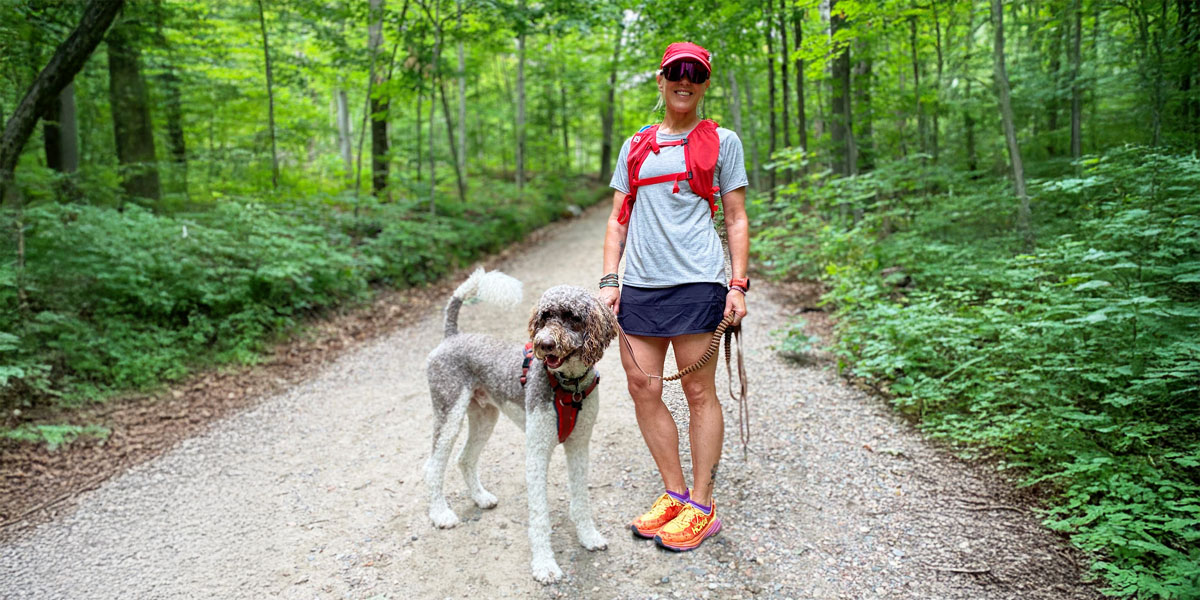 woman in running gear smiling and posing with her dog