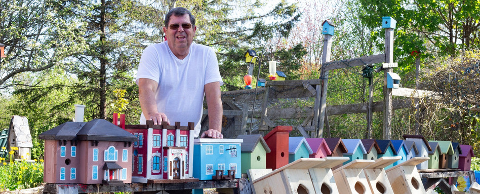 man smiling behind a table with birdhouses on it
