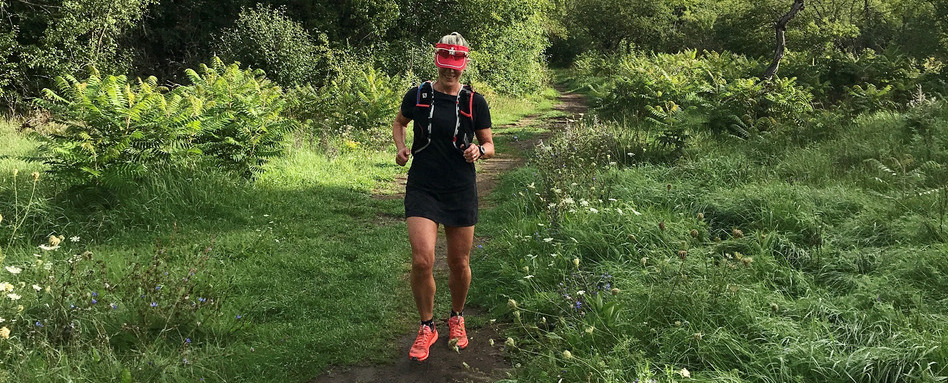 woman running on a trail with greenery behind
