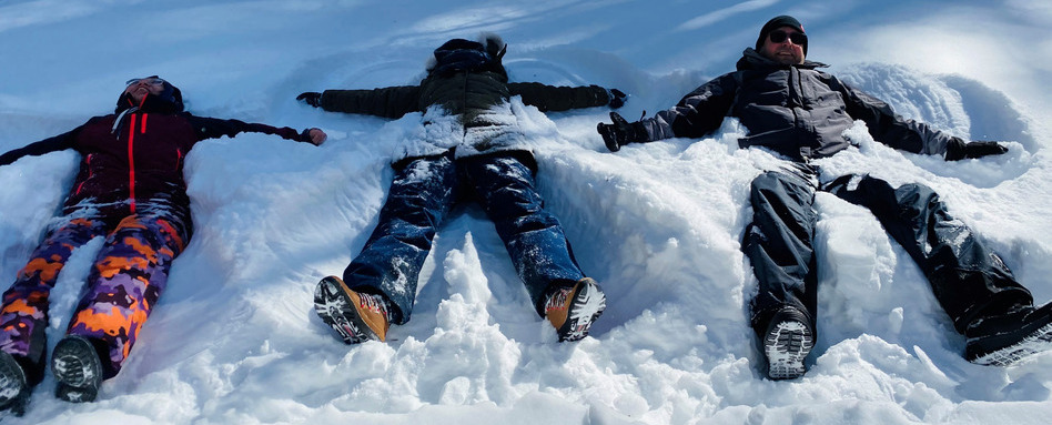 people lying in the snow smiling on a sunny day
