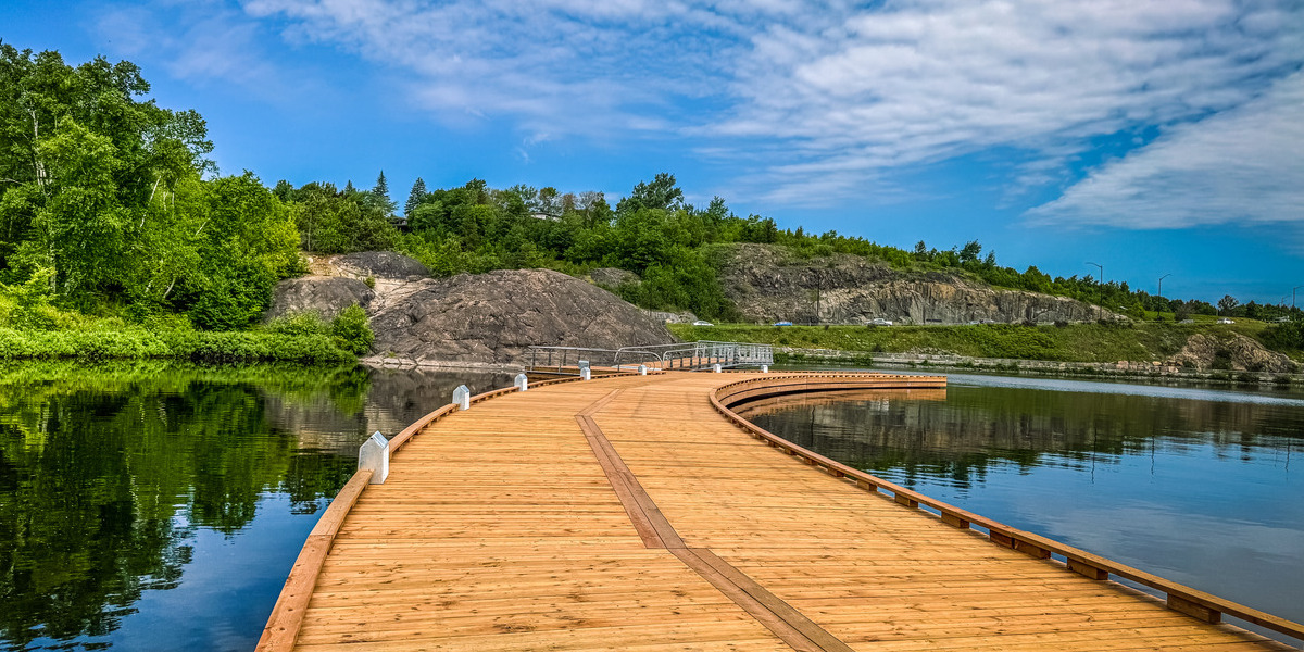 wooden walkway over body of water with blue skies and forest behind