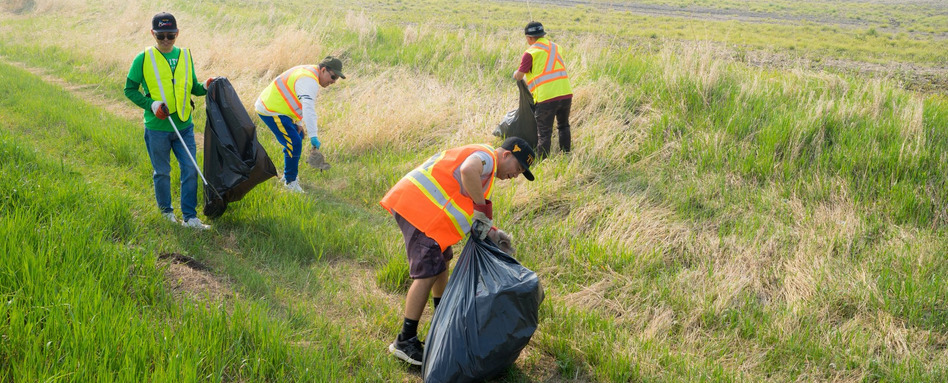 people in hazard vests cleaning trash in a field