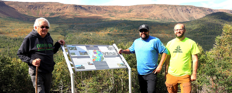 Three people standing next to a sign, smiling at the camera.