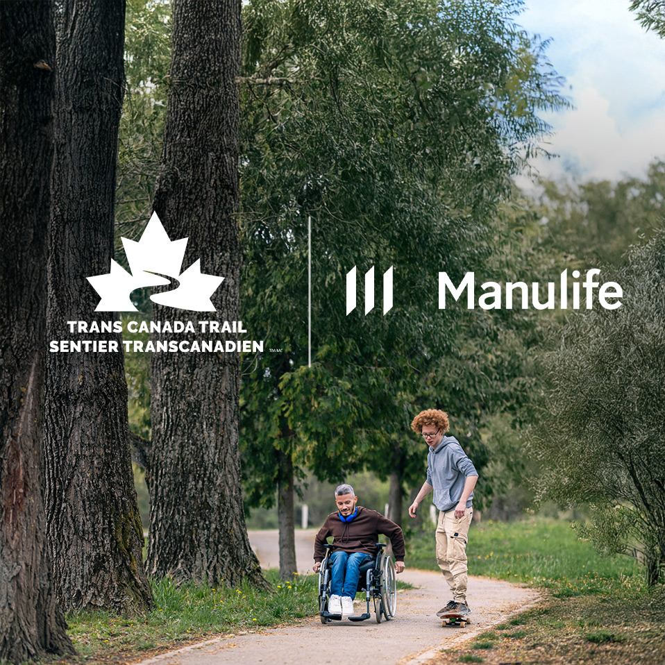 person in wheelchair with person walking in forest on trail