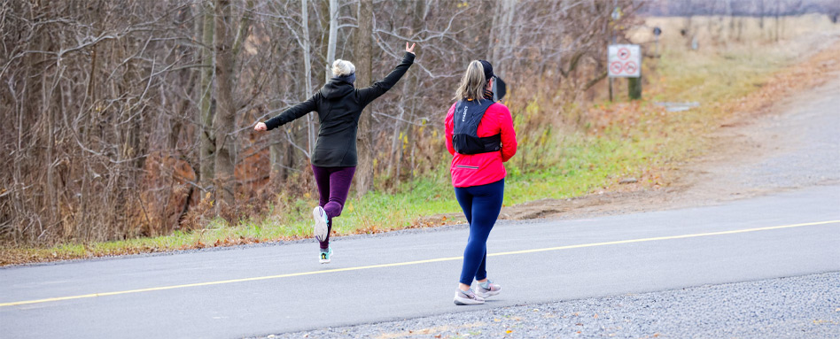 Two people walking, seen from behind. The person on the left is leaping in the air with arms outstretched.
