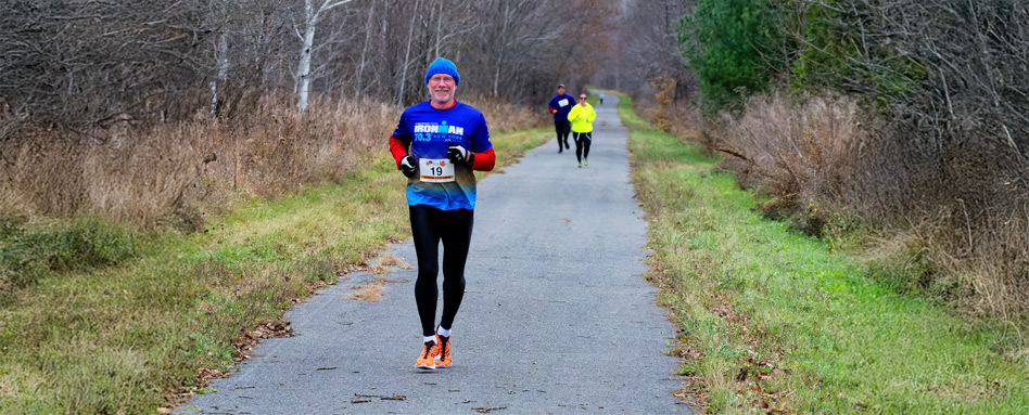 Man dressed in blue, running down a trail, smiling.