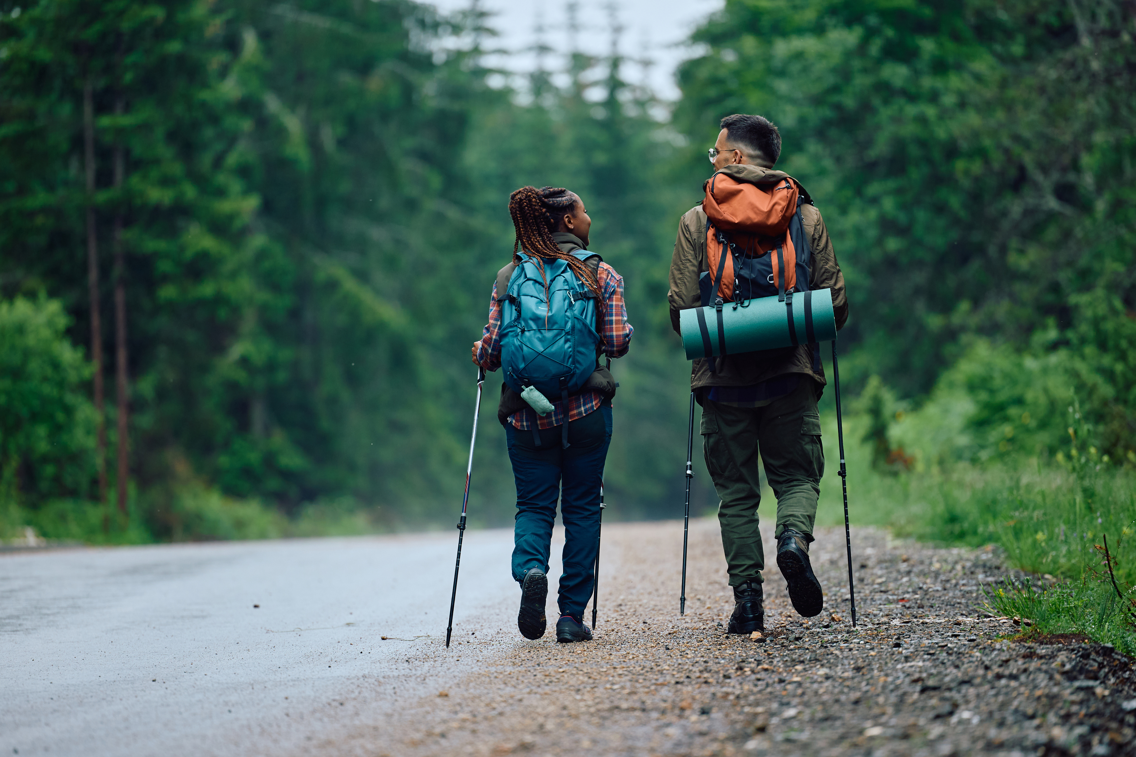 Back view of couple of hikers enjoying in a walk in nature by the road.
