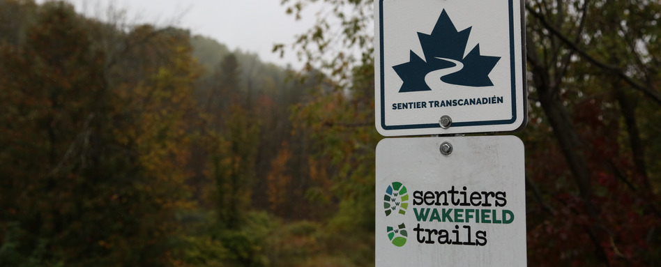 QC_Web story_Volunteer recognition Ken Bouchard_credit David Chan | Trans Canada Trail A sign reading Sentier Transcanadien sits about a sign reading Sentiers Wakefield Trails