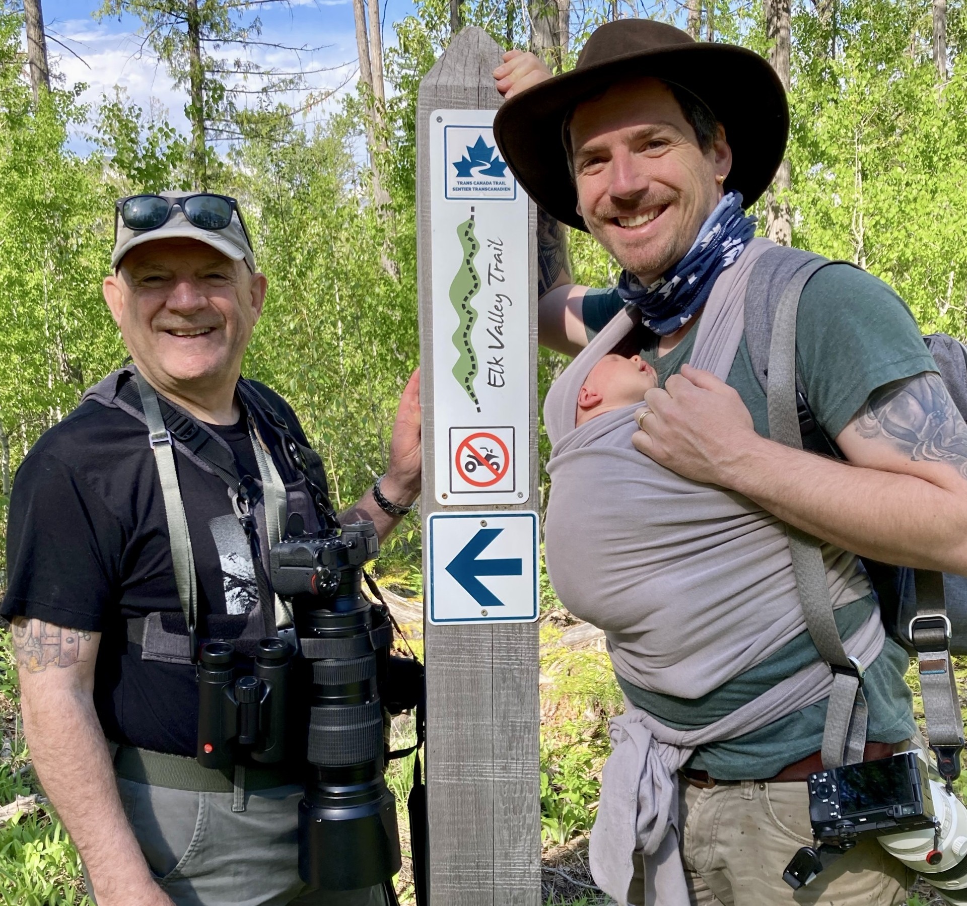 two men and a babh smiling on a trail on a sunny day