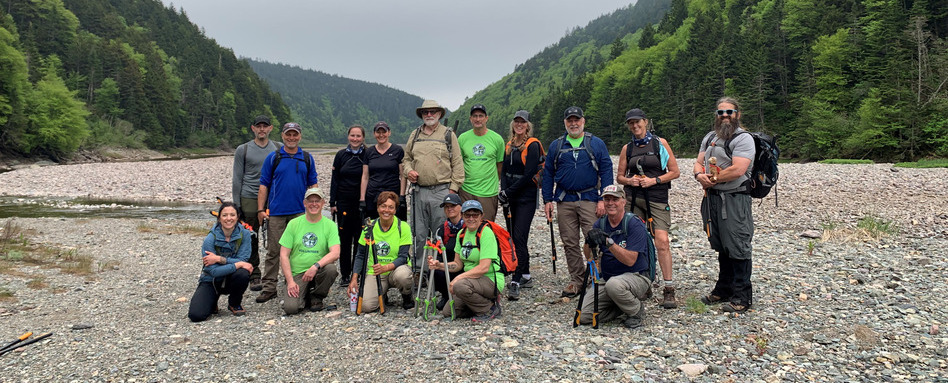 01Support image_NB_Fundy Trail_SF107809_NB_Trail-Care-2025-Fundy-Hiking-Trail-Association | Trans Canada Trail group of people in matching tshirts standing on gravel with tools and mountains behind