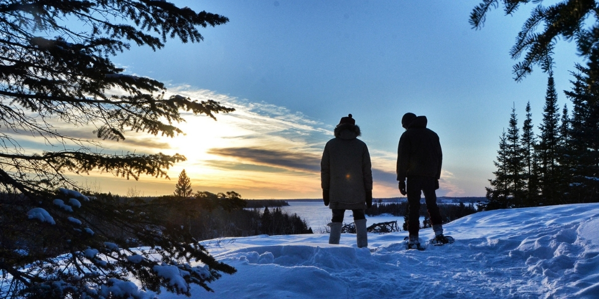 two people standing in the snow overlooking a sunset