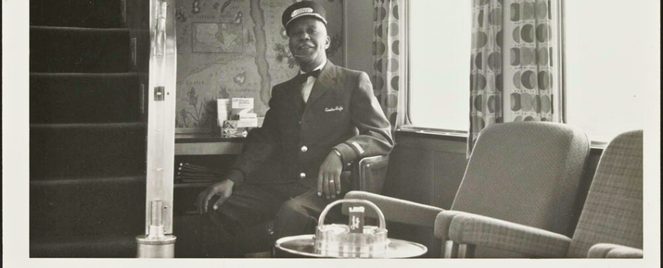 02Support image_Under Lee Atwell section_credit Library and Archives Canada | Sentier Transcanadien A man looking at the camera, wearing a sleeping car porter uniform, sitting in a train car.