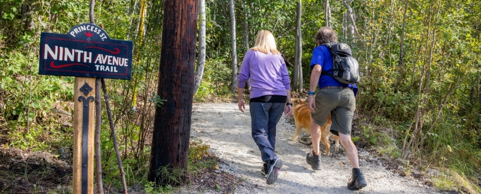 man, woman and dog walking on wooded trail
