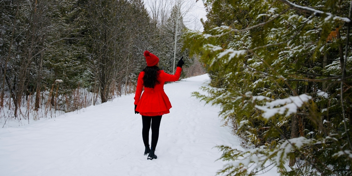00Feature image_ON_Caledon Trailway_credit Travels with Asavari | Trans Canada Trail woman in red dress walking on a snow covered trail in forest