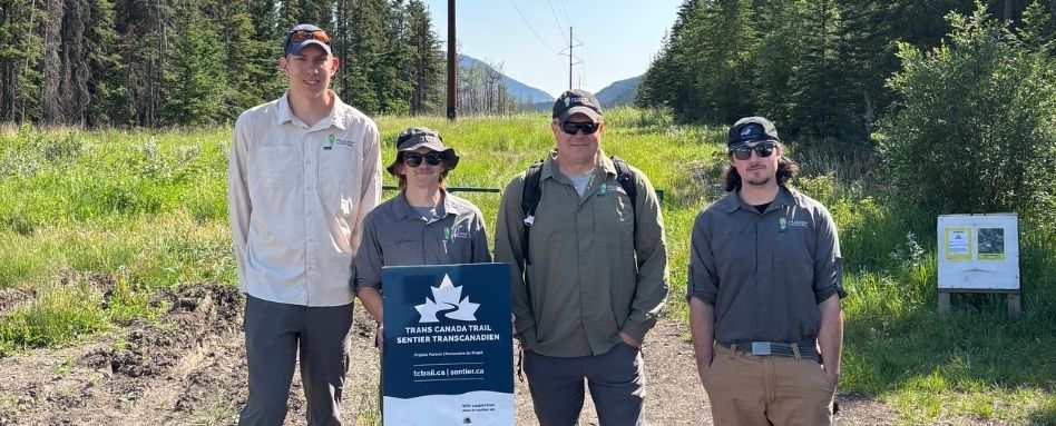 02Support image_AB_107672-Friends of Kananaskis_web story_sign | Trans Canada Trail people holding a trail sign smiling on sunny day