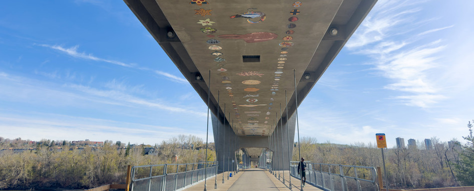 A concrete pedestrian bridge. Guardrails are on both sides and the overpass is decorated with several small art pieces.