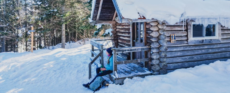 woman sitting on log cabin steps on a snowy day