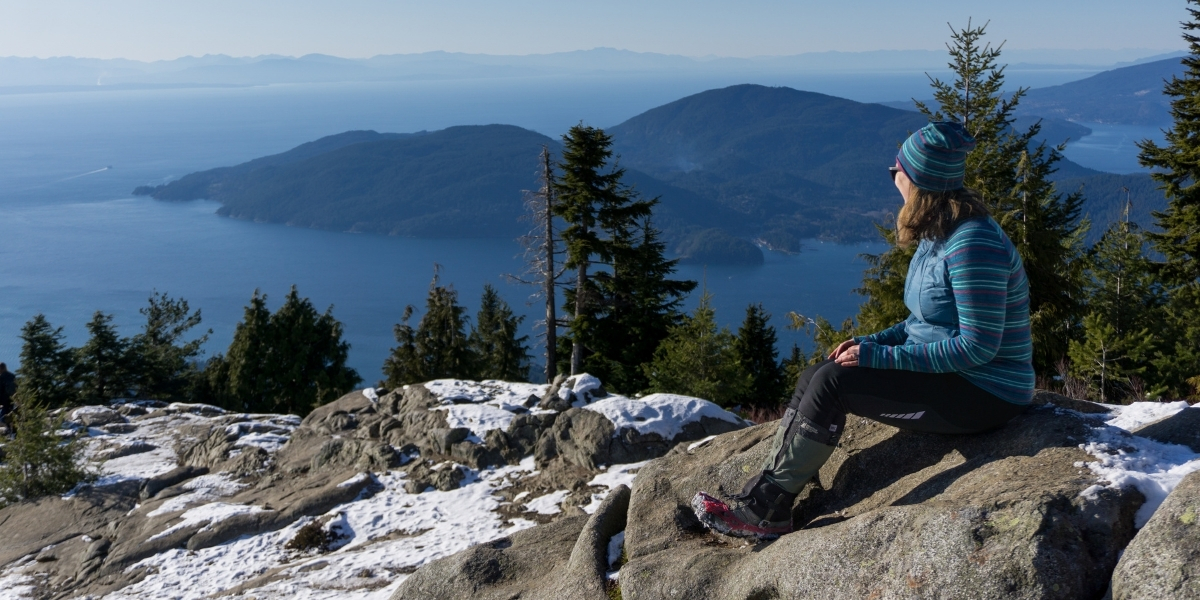 00Feature image_BC_nonTCT_credit Taryn Eyton | Trans Canada Trail woman sitting atop a snowy montain on a sunyn day overlooking lake and mountains