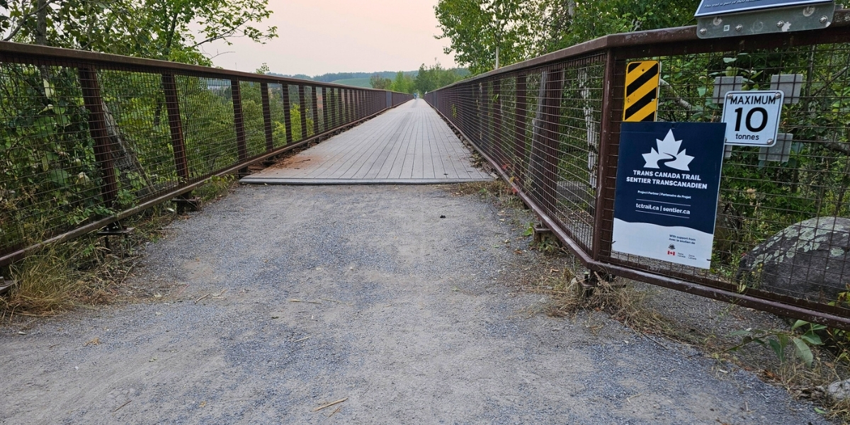 00Feature image_ON_Web story_Kawartha Doubes Bridge_credit Kawartha Trans Canada Trail Association | Trans Canada Trail large bridge with trail signage looking toward cloudy sunset