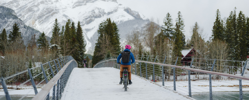 Rear view of man on mountain bike across the bridge in Banff in winter