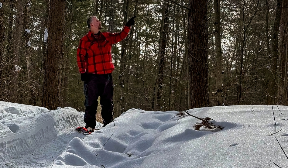 man standing on snowshoes pointing to forest