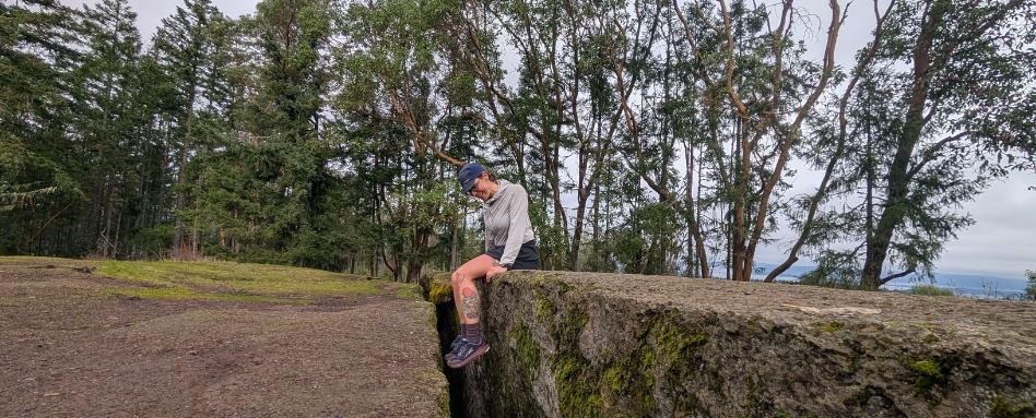 person sitting on large rock in hiking gear on cloudy day