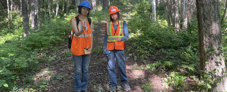 two girls showing a peace sign in hazard gear in forest