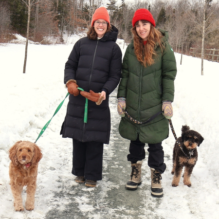 two girls walking dogs smiling on a snowy trail