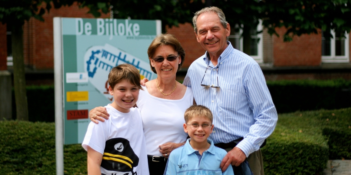 a husband and wife pose with their two sons smiling on a sunny day
