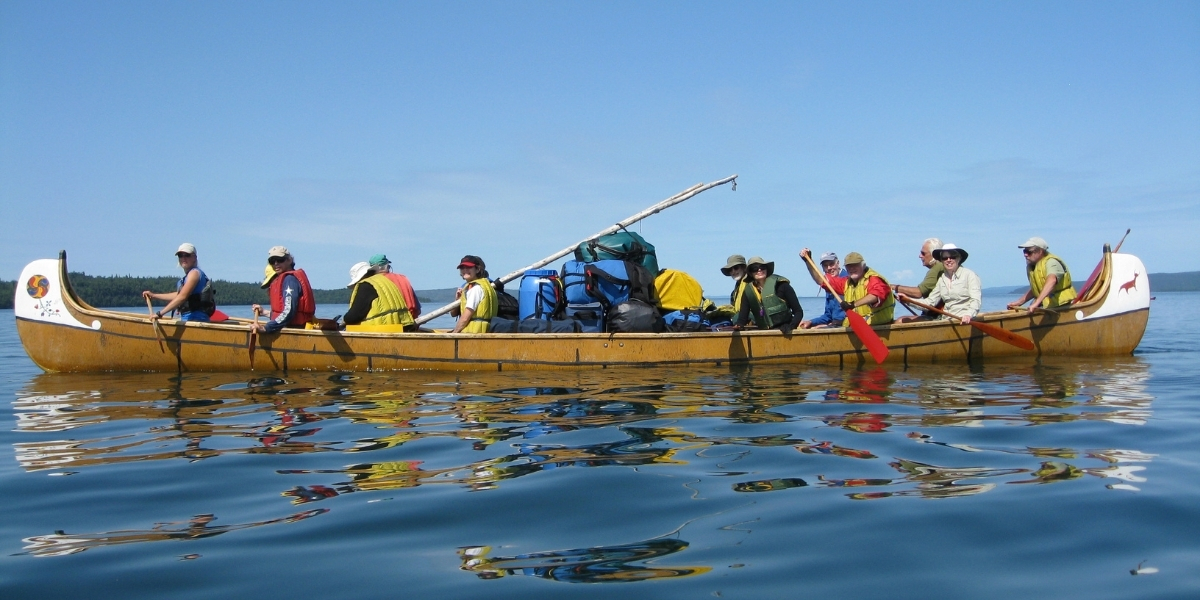 people in a large canoe paddling on a lake on a sunny day
