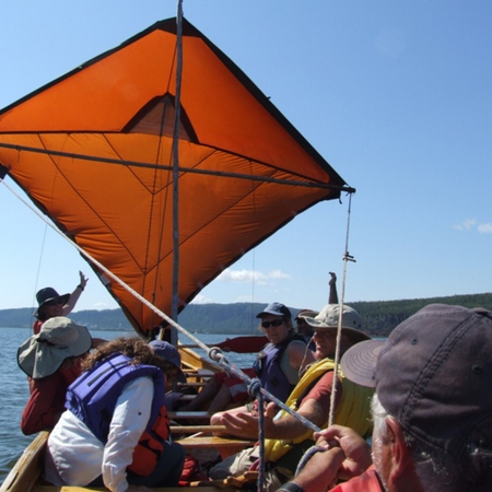 large orange sail with people on a boat on a sunny day