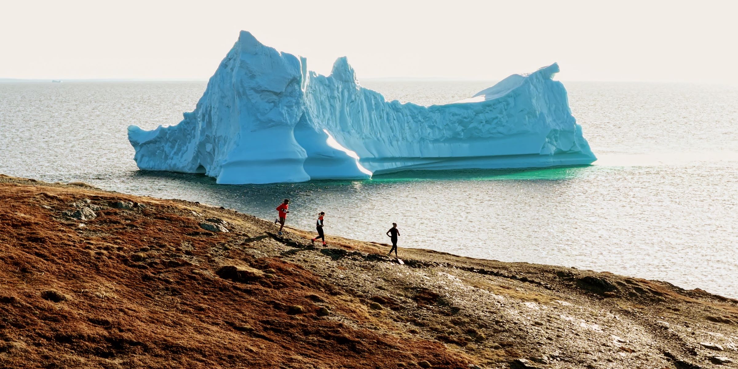 Trail Run Photo-GNT-webcrop | Trans Canada Trail People run on the Atlantic coast along the Great Northern Trail with an iceberg in the background.