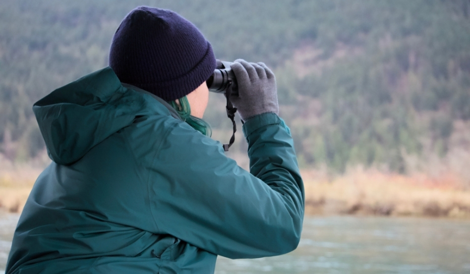 person using binoculars looking out to lake and forest