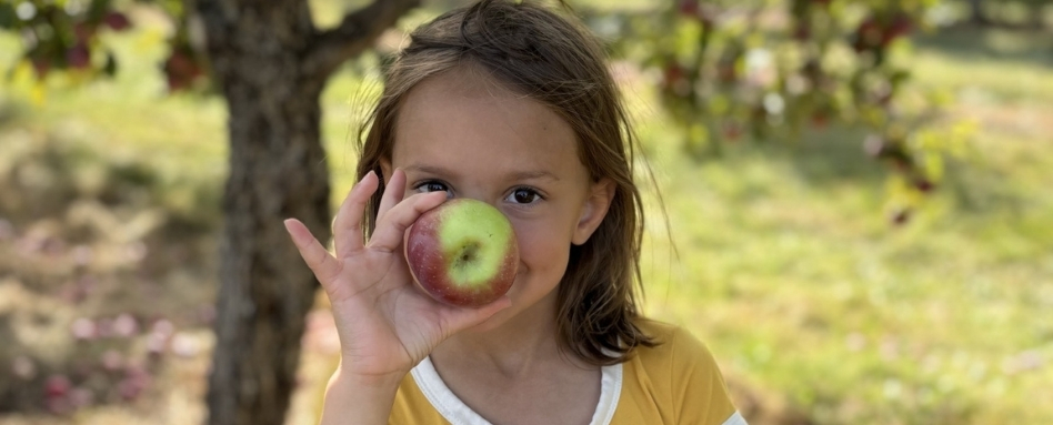 child smiling and holding an apple up to her face
