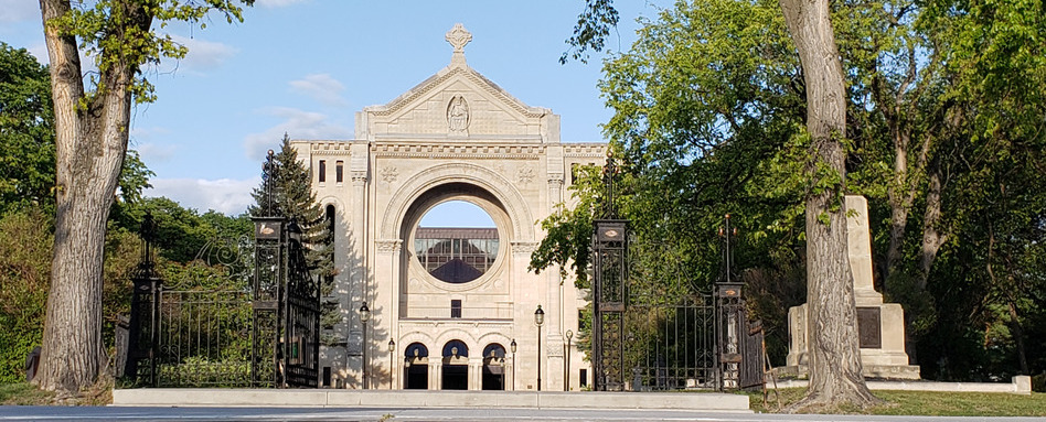 Historic stone arch gateway with a circular central opening, framed by trees in a park setting.