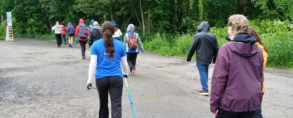 Group of hikers walking along a gravel trail in a forest, many with backpacks and rain gear.