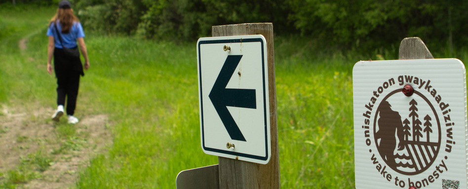 02Support image_Onishaktoon Gwaykaadiziwin_photo credit Keely Middleton kbphoto | Trans Canada Trail trail signage behind a woman walking in a field