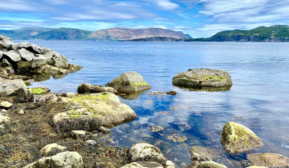 large boulders in waterfront with rolling mountains behind