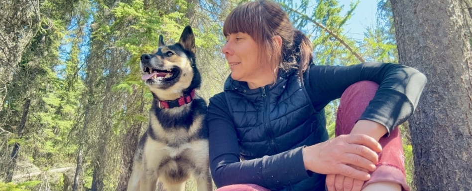 A woman and her dog sitting down. The woman is looking at her dog. It is a sunny day.