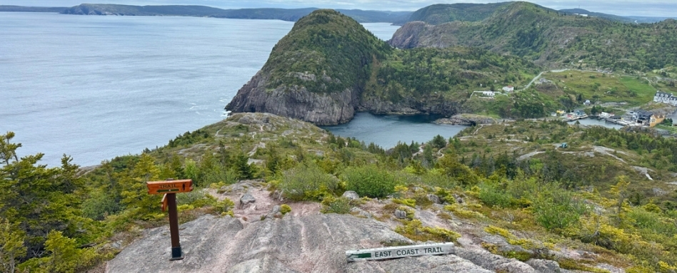 02Support image_NL_East Coast Trail Taryn Eyton_credit Taryn Eyton | Trans Canada Trail A hiking path at Quidi Vidi. A sign reading East Coast Trail is placed in the centre of hte image. Grassy cliffs and the ocean are in the background.