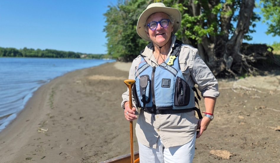 03Support image_Blue Trails NB_credit Cathy Donaldson_Moon | Trans Canada Trail Older woman in a life jacket holding a wooden paddle on a sunny riverside beach