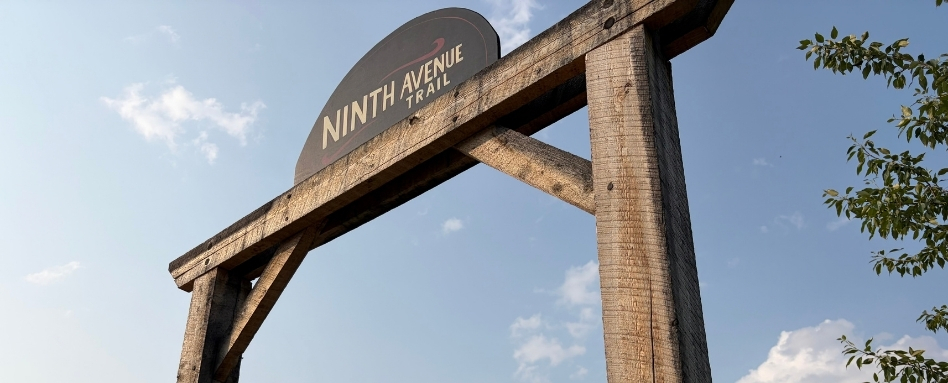 Wooden trail entrance sign reading'Ninth Avenue Trail' against a clear blue sky.