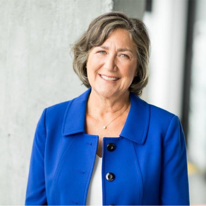 Smiling middle-aged woman in a royal blue blazer standing against a light wall, portrait photo.